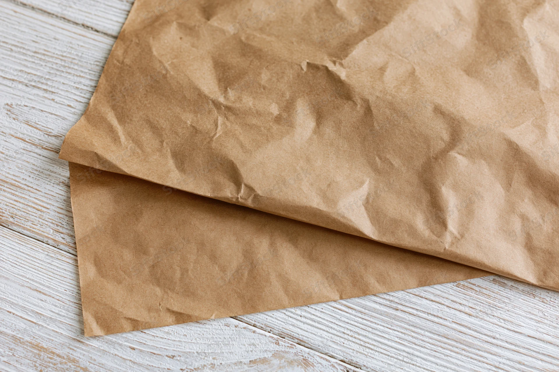 Crumpled brown paper sheets on a white weathered wooden surface