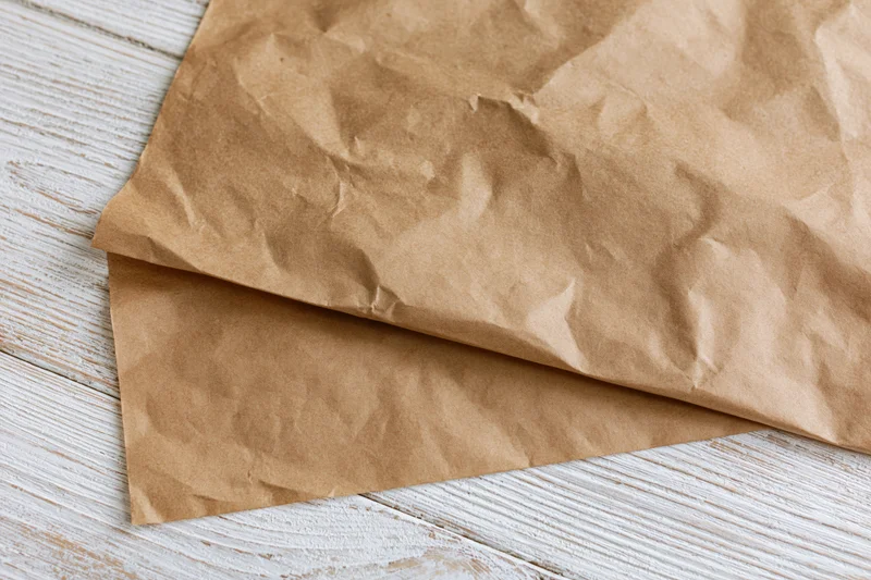 Crumpled brown paper sheets on a white weathered wooden surface