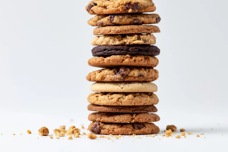 Stack of assorted cookies arranged vertically on white background with crumbs scattered around