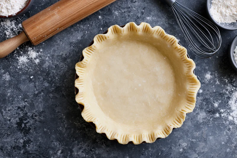 Uncooked pie crust in a fluted pan on a dark countertop surrounded by baking tools and flour