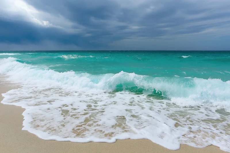 Turquoise ocean waves breaking on sandy beach under stormy sky