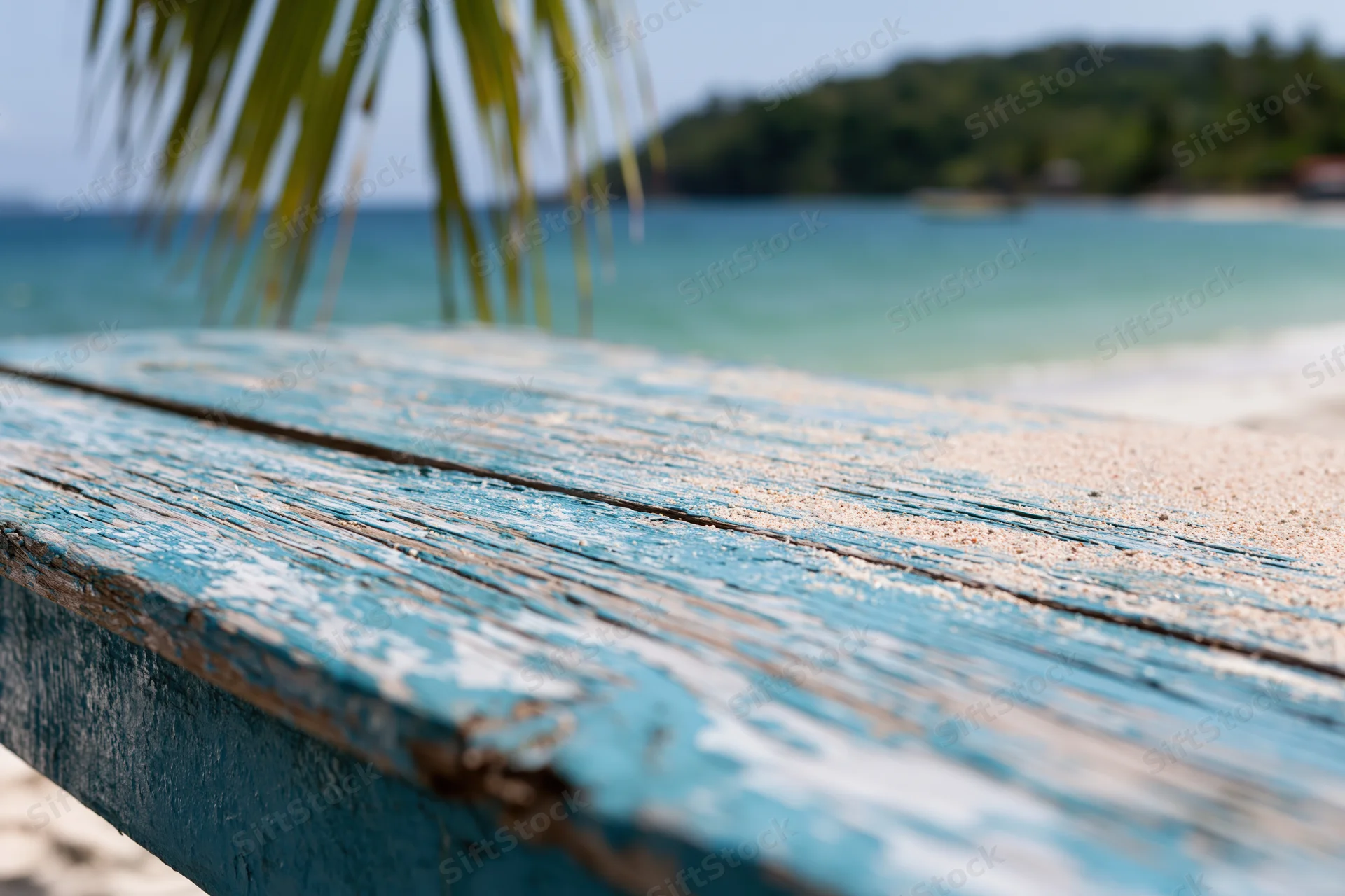 Weathered blue wooden table on a sandy beach with ocean and palm fronds in the background