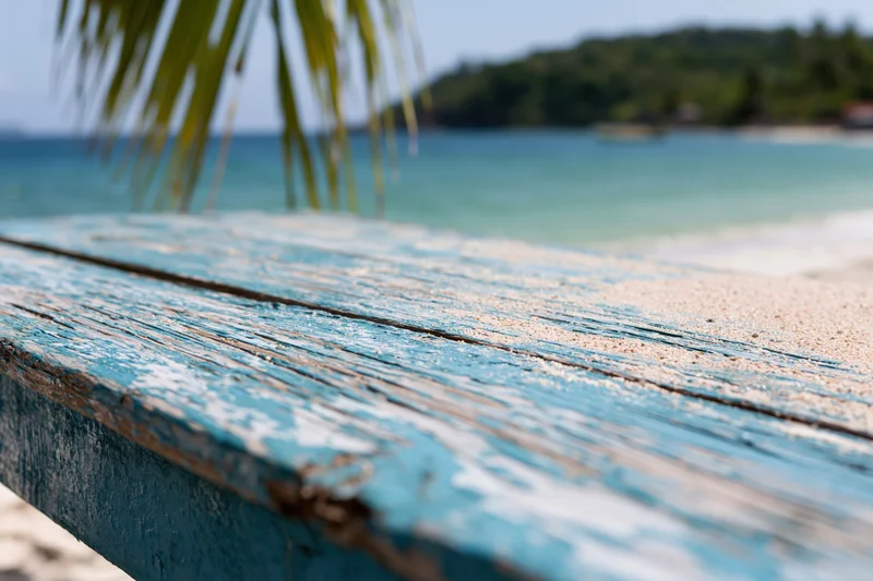 Weathered blue wooden table on a sandy beach with ocean and palm fronds in the background