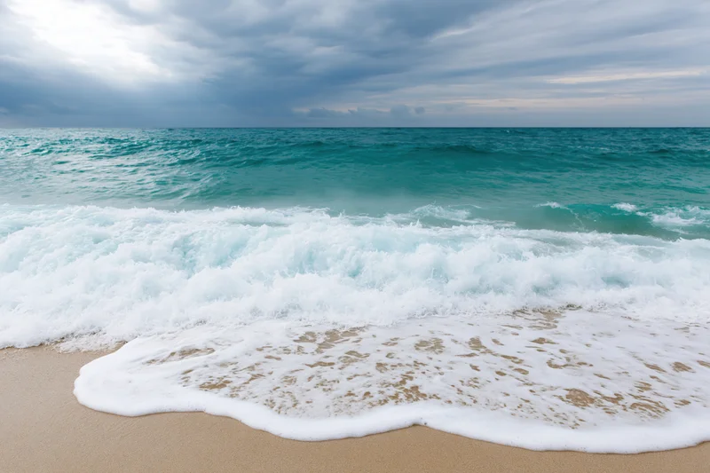 Waves breaking on sandy beach under cloudy sky