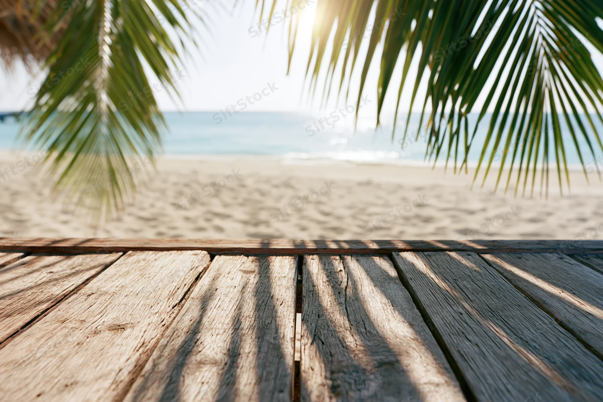 Wooden deck overlooking sandy beach with palm fronds and ocean in background