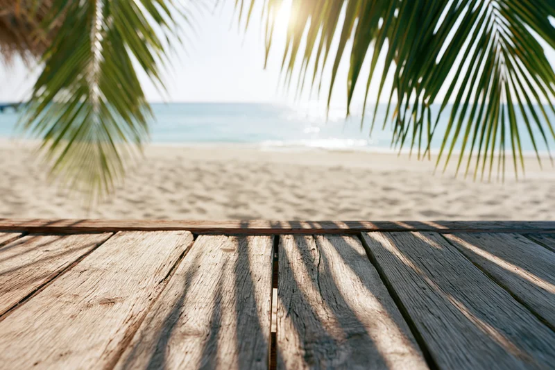 Wooden deck overlooking sandy beach with palm fronds and ocean in background