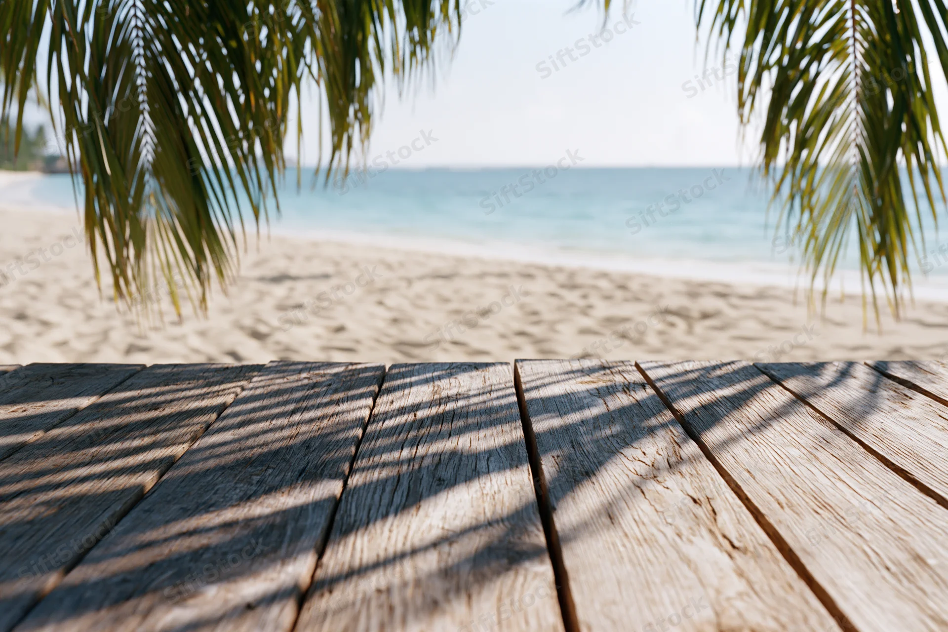Wooden deck with palm fronds framing a sandy beach and ocean view
