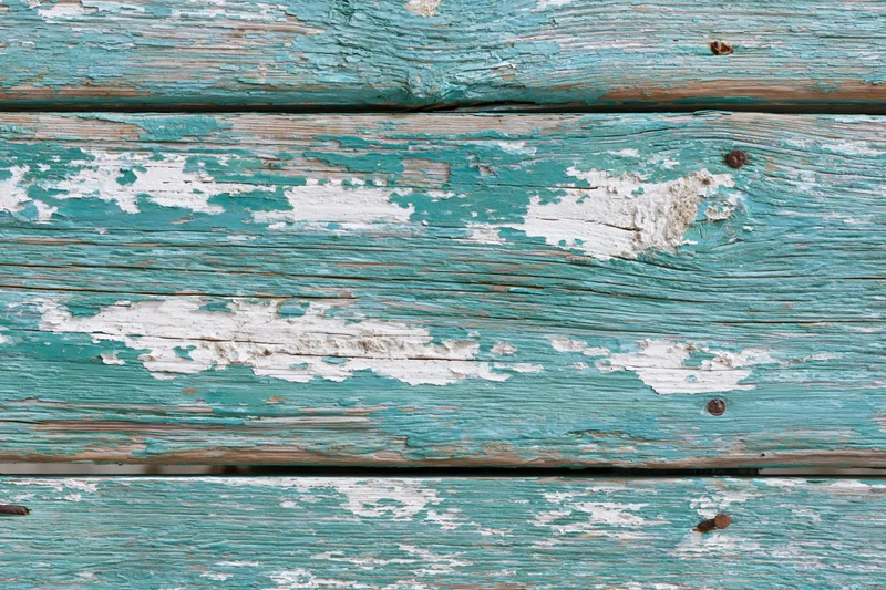 Weathered wooden planks with peeling turquoise and white paint, showing grain and nails