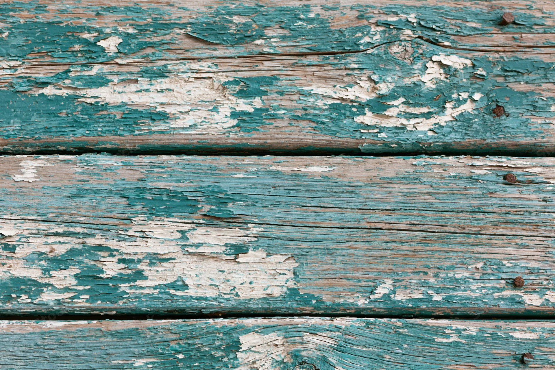 Weathered wooden planks with peeling teal and white paint, showing grain and cracks