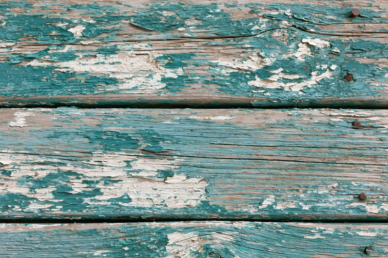 Weathered wooden planks with peeling teal and white paint, showing grain and cracks