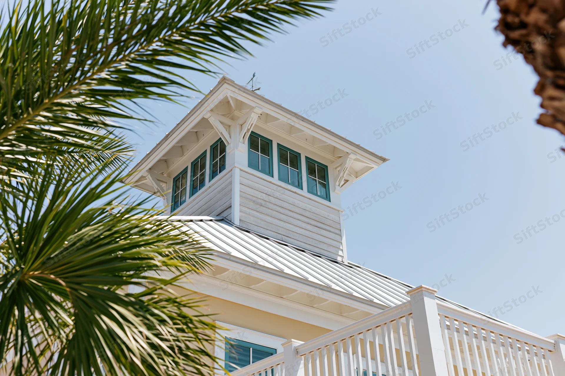 White coastal house with blue windows and palm fronds framing the tower under clear sky