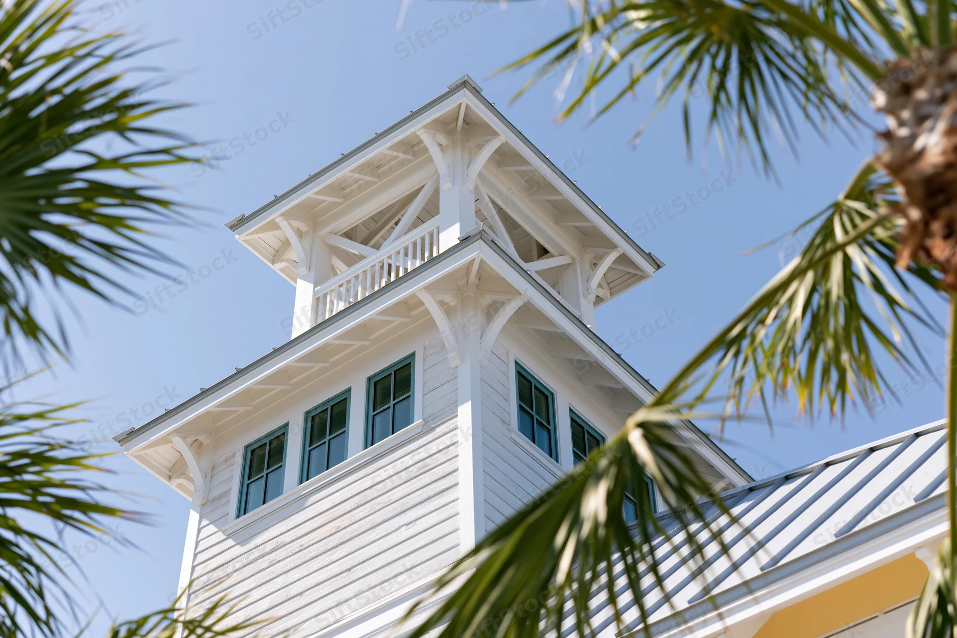 White wooden tower with teal windows and palm fronds framing the view against a blue sky