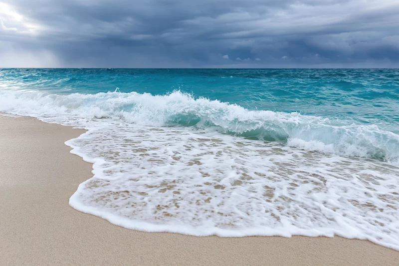 Waves breaking on sandy beach under cloudy sky