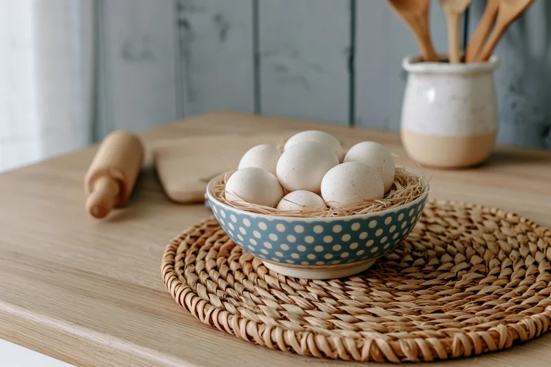 Eggs in a polka dot bowl on a woven placemat on a wooden kitchen table