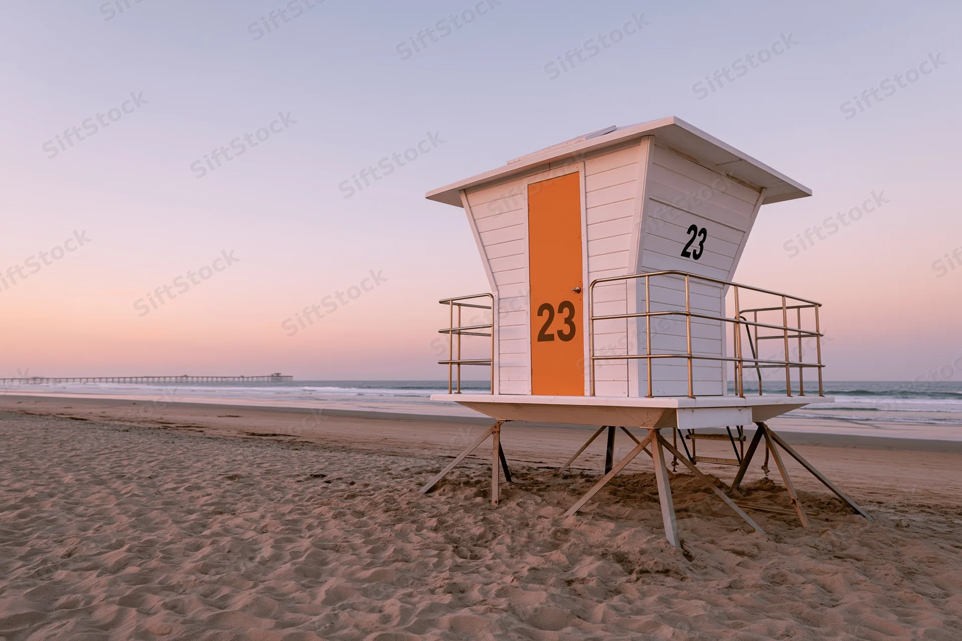 White lifeguard tower with orange door and number 23 on sandy beach at sunset near ocean