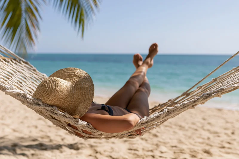 Woman reclining in a hammock on a sandy beach with ocean view