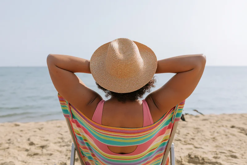Woman relaxing in a striped deckchair on the beach with arms behind head, facing the ocean