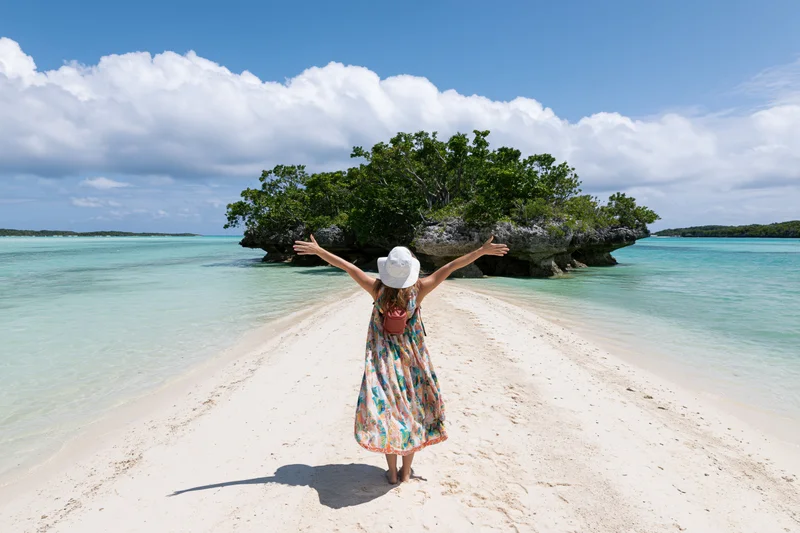 Woman standing on sandy beach with arms outstretched facing tropical island and turquoise water