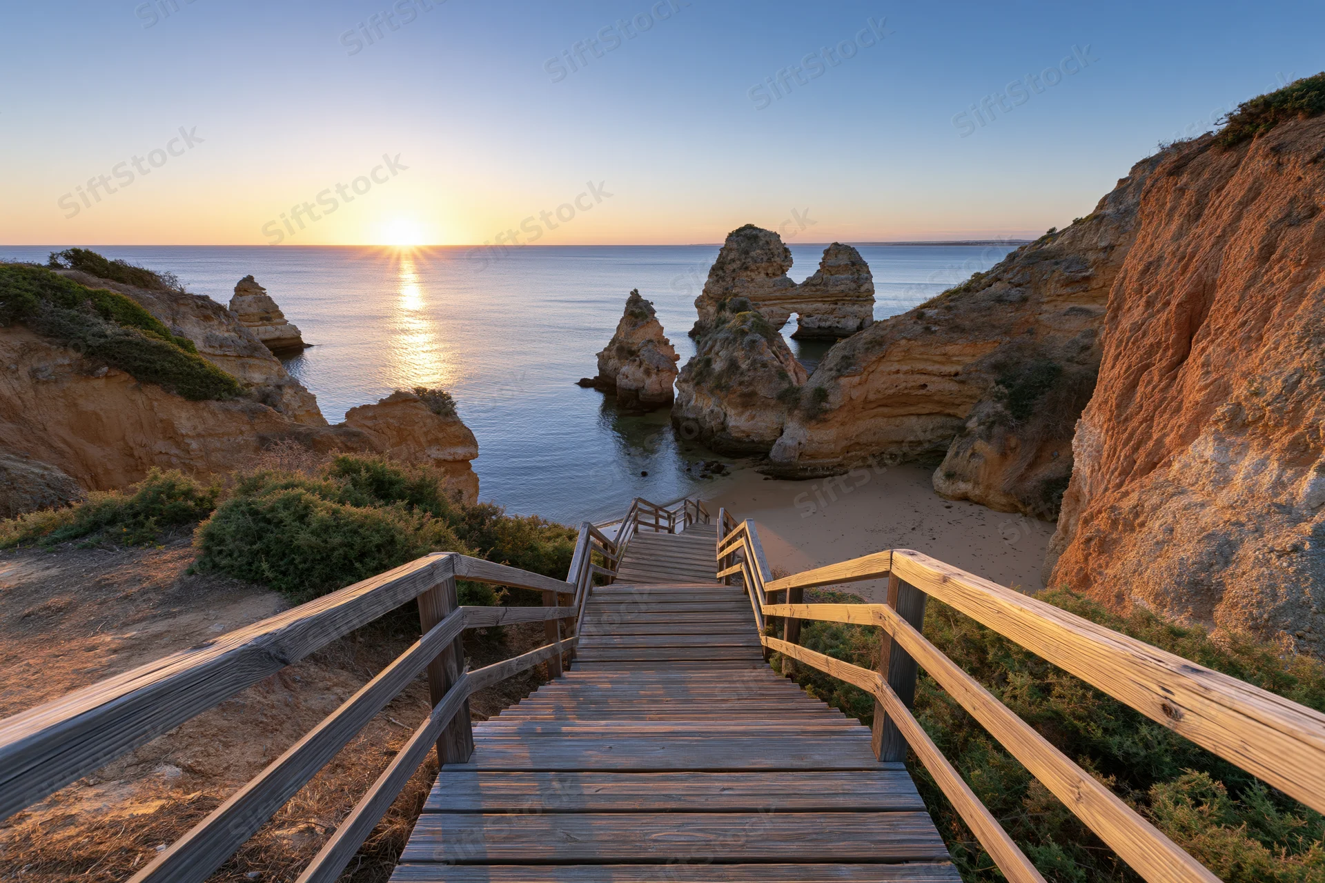 Wooden staircase descending to a secluded beach at sunset between coastal cliffs