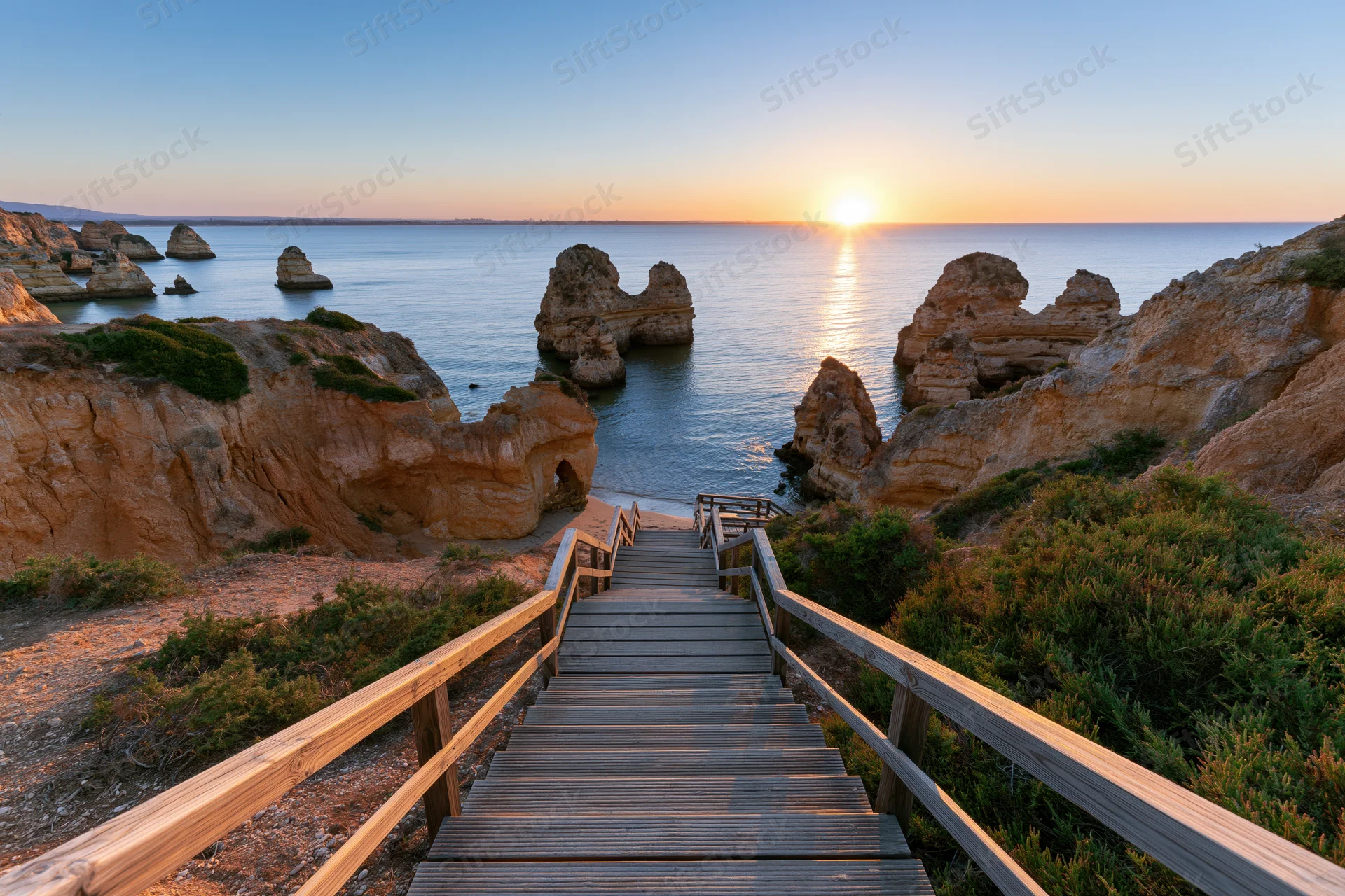 Wooden staircase descending to ocean at sunset between rocky cliffs