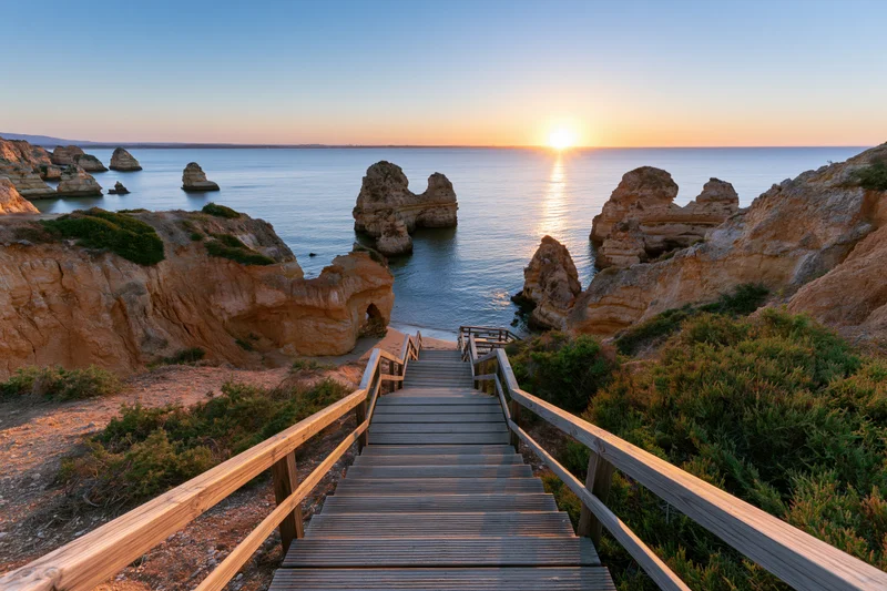 Wooden staircase descending to ocean at sunset between rocky cliffs