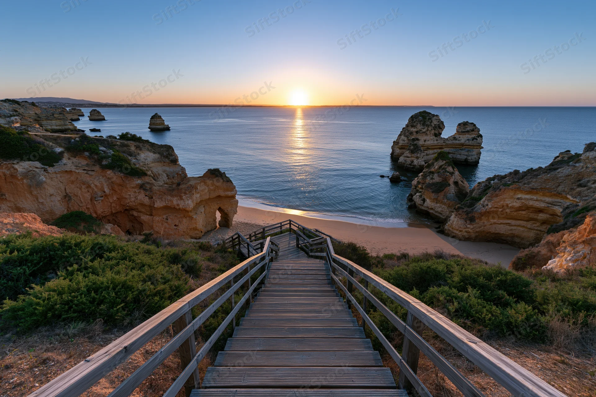 Wooden staircase descending to a sandy beach at sunset between coastal cliffs and the ocean