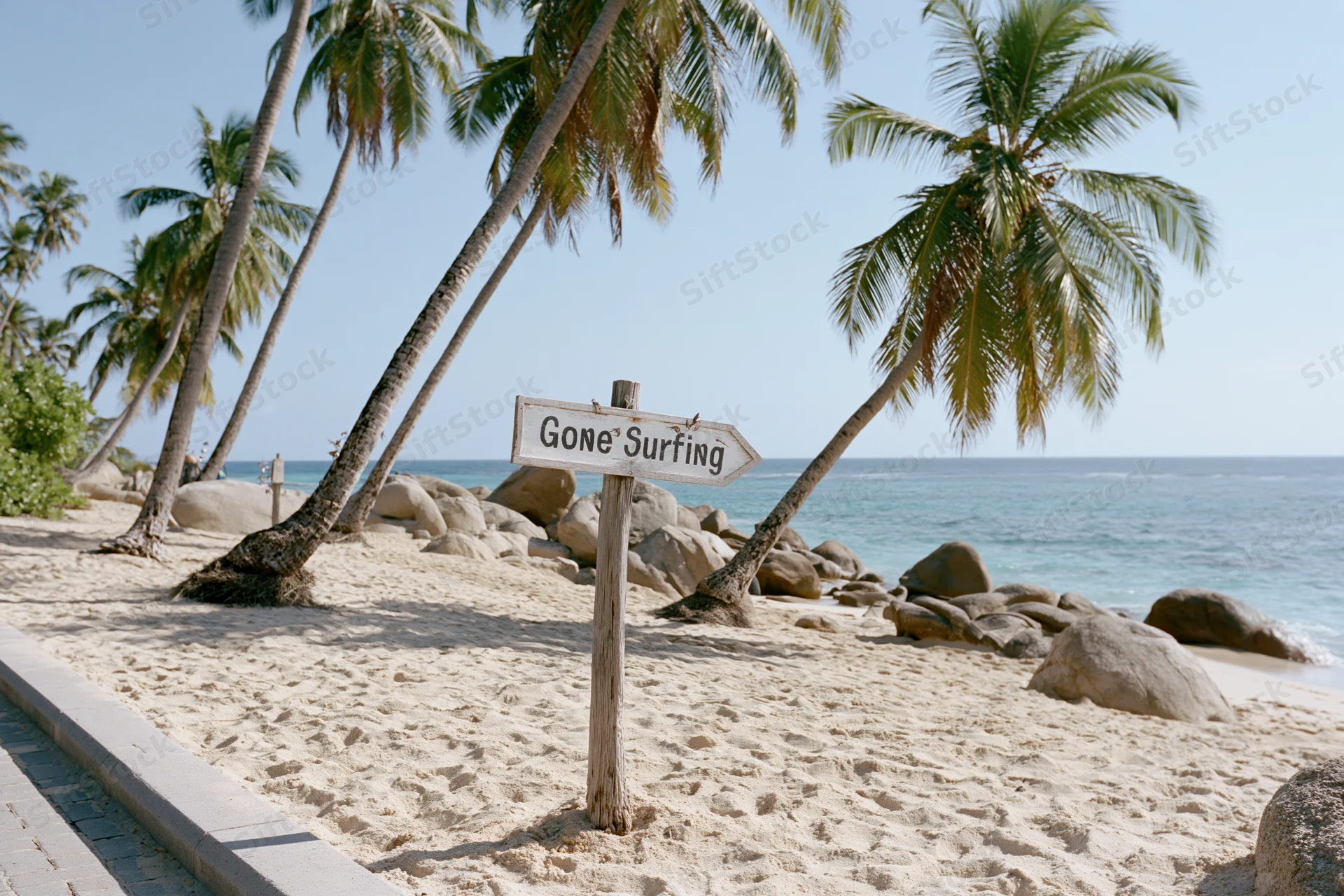 Wooden sign reading gone surfing on sandy beach with palm trees and ocean in background