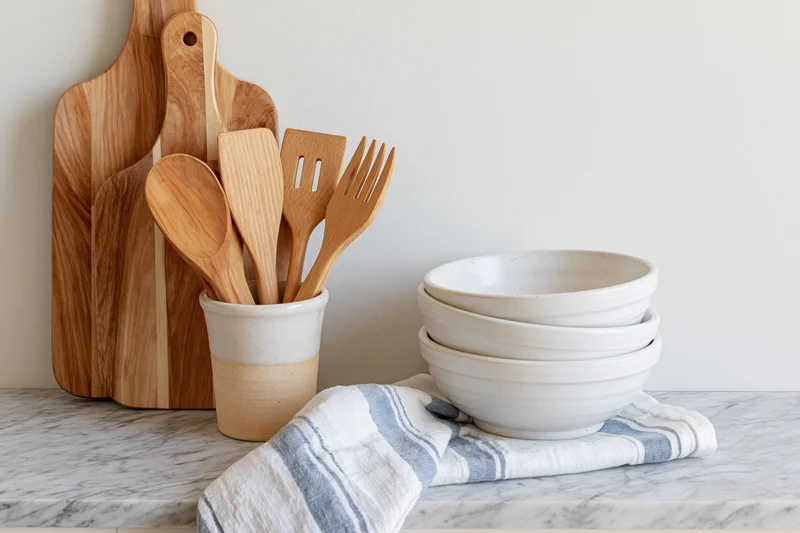 Wooden kitchen utensils and ceramic bowls arranged on a marble countertop with a striped towel