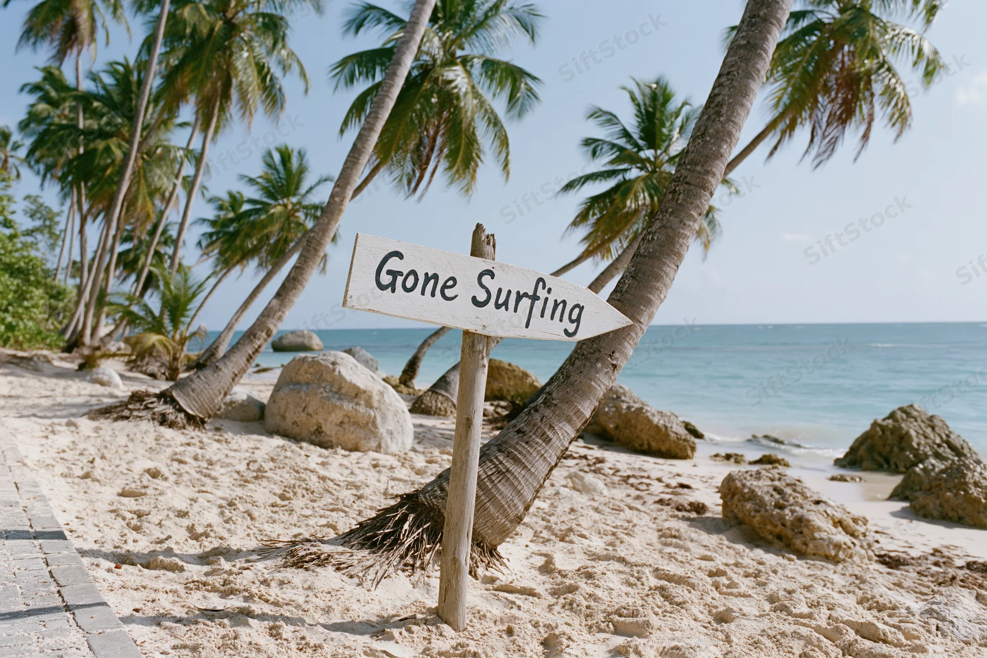 Wooden sign reading gone surfing on sandy beach with palm trees and ocean in background