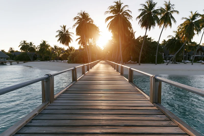 Wooden pier extending over calm ocean toward tropical beach at sunset