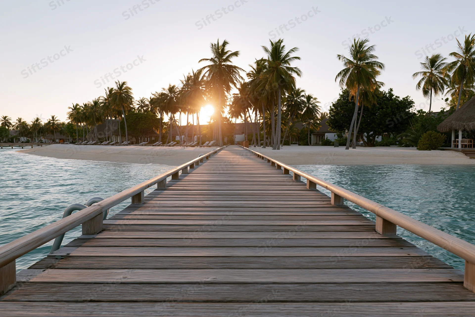 Wooden dock leading to tropical beach at sunset with palm trees and ocean on either side