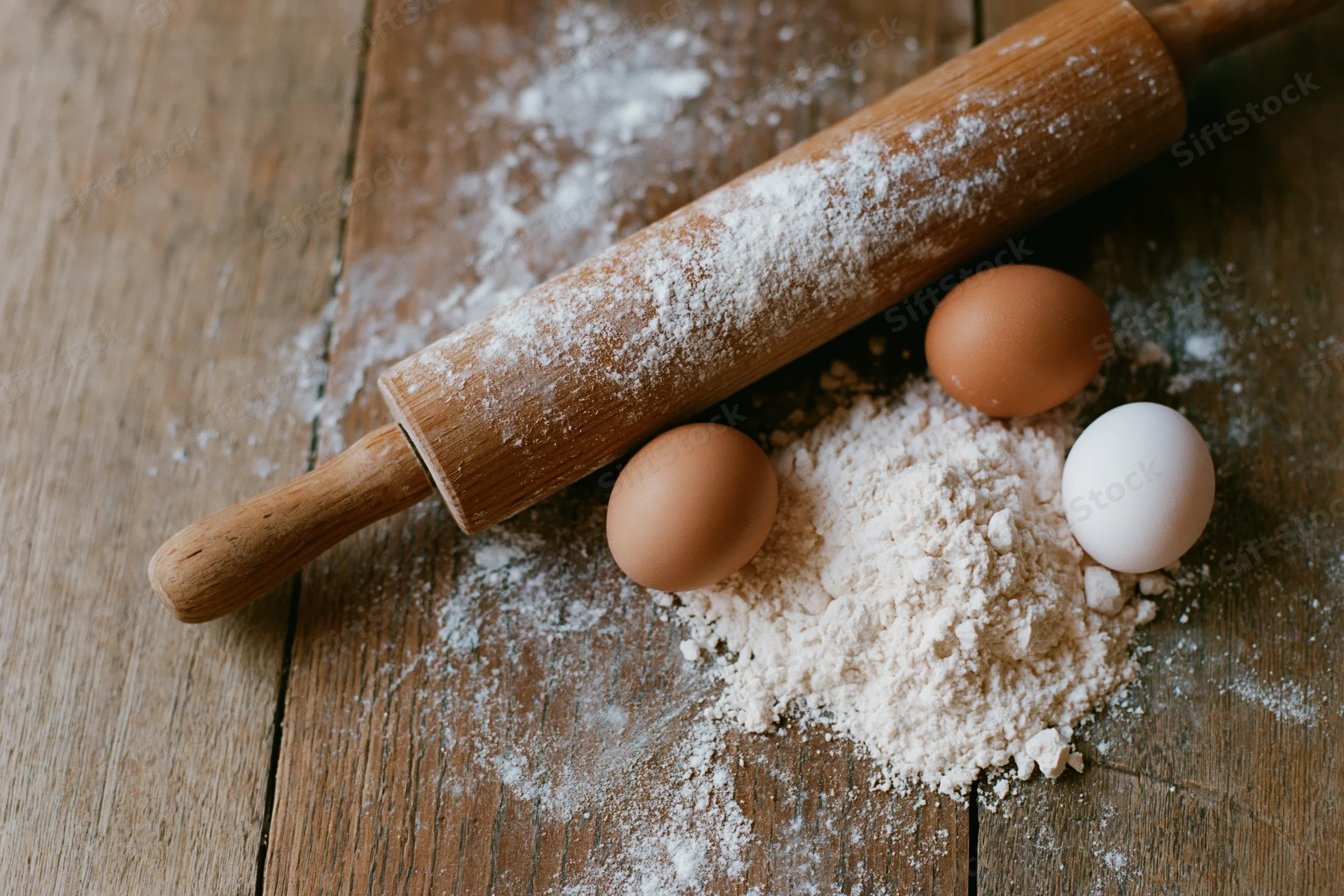 Wooden rolling pin and eggs with flour on a rustic kitchen table