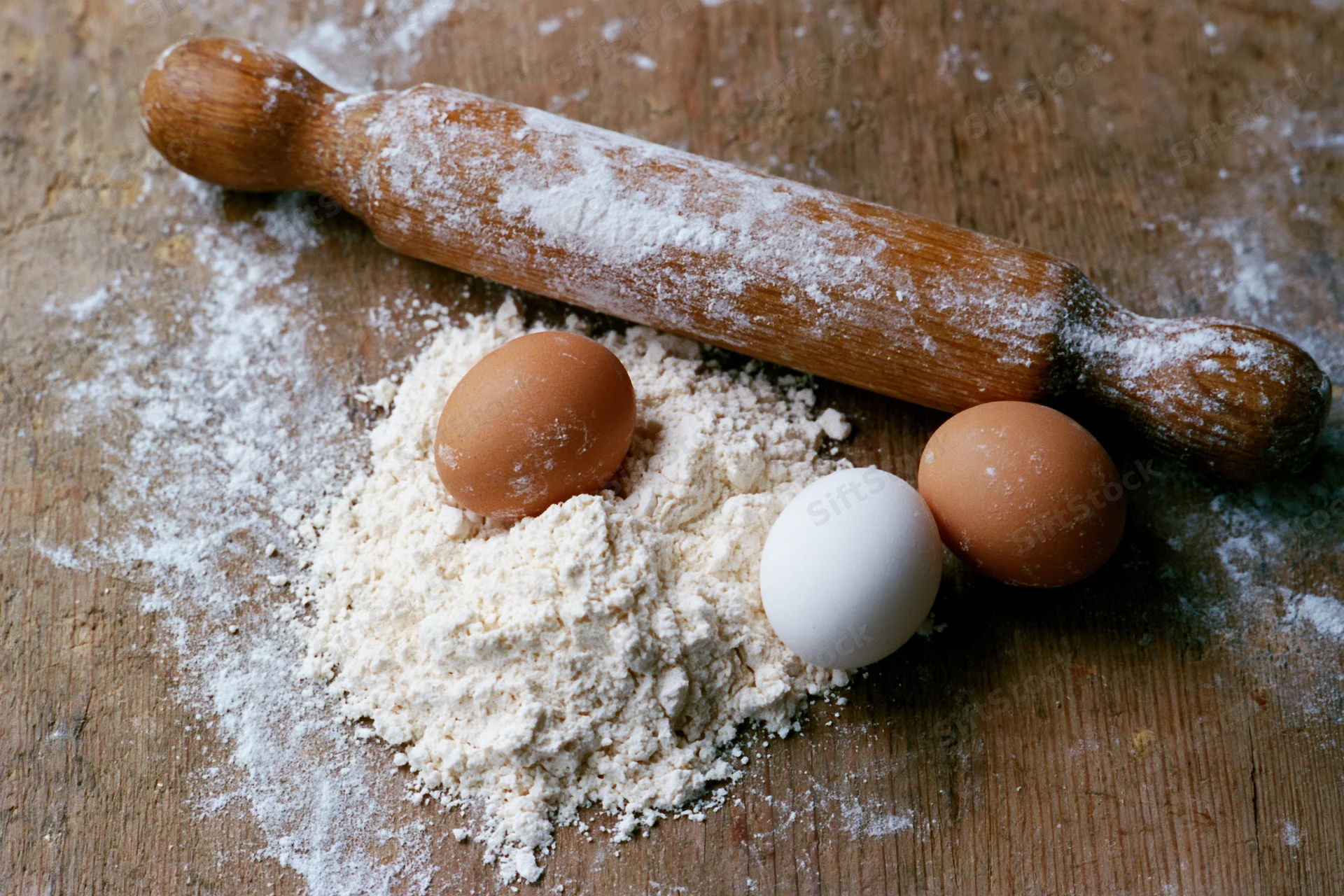 Flour and eggs with a wooden rolling pin on a rustic kitchen countertop