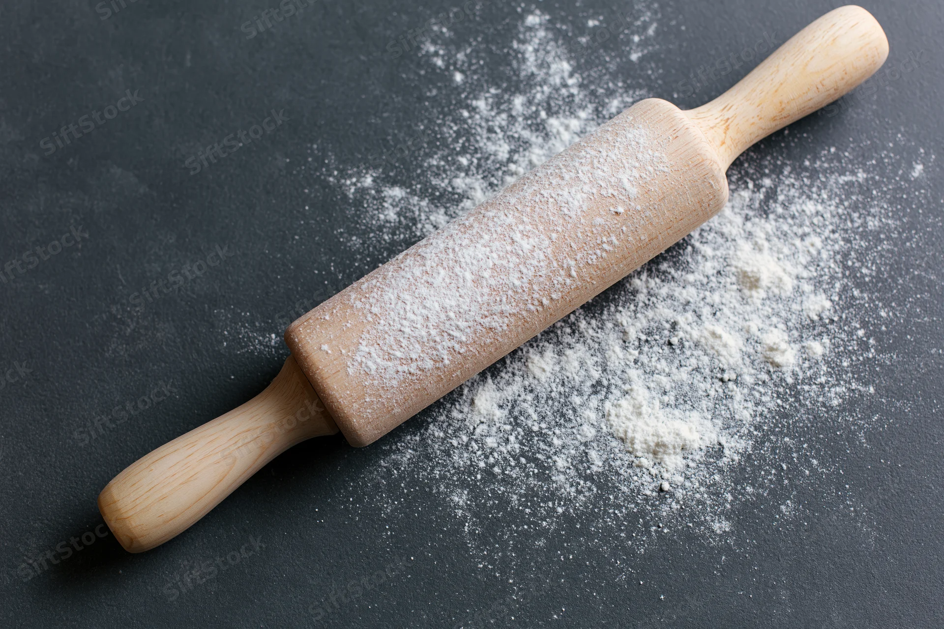 Wooden rolling pin dusted with flour on dark countertop