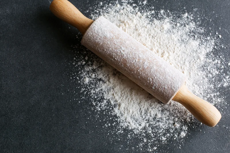 Wooden rolling pin dusted with flour on dark countertop