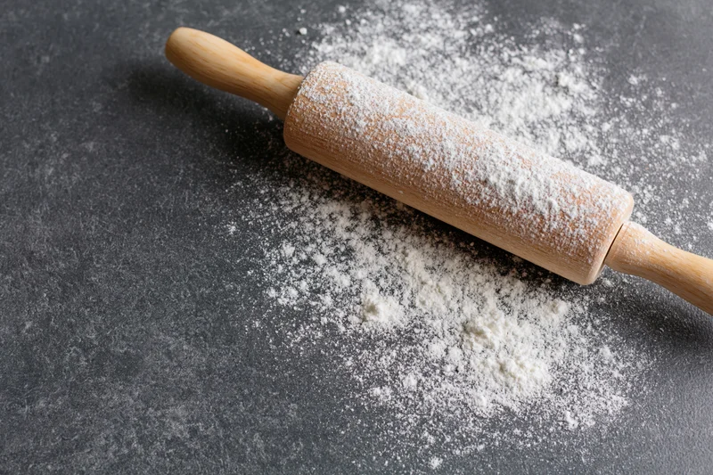 Wooden rolling pin dusted with flour on dark countertop