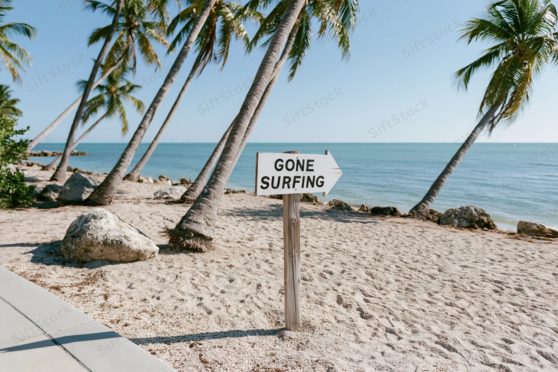 Wooden sign reading gone surfing on sandy beach with palm trees and ocean in background