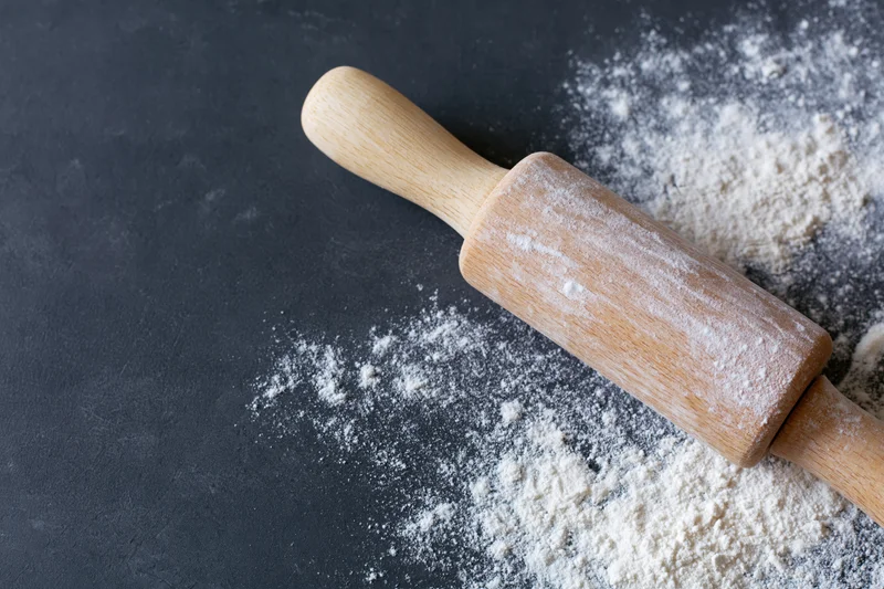 Wooden rolling pin dusted with flour on dark countertop