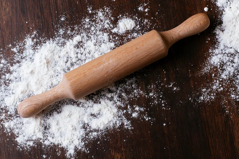 Wooden rolling pin resting on a floured dark wood surface in a kitchen setting
