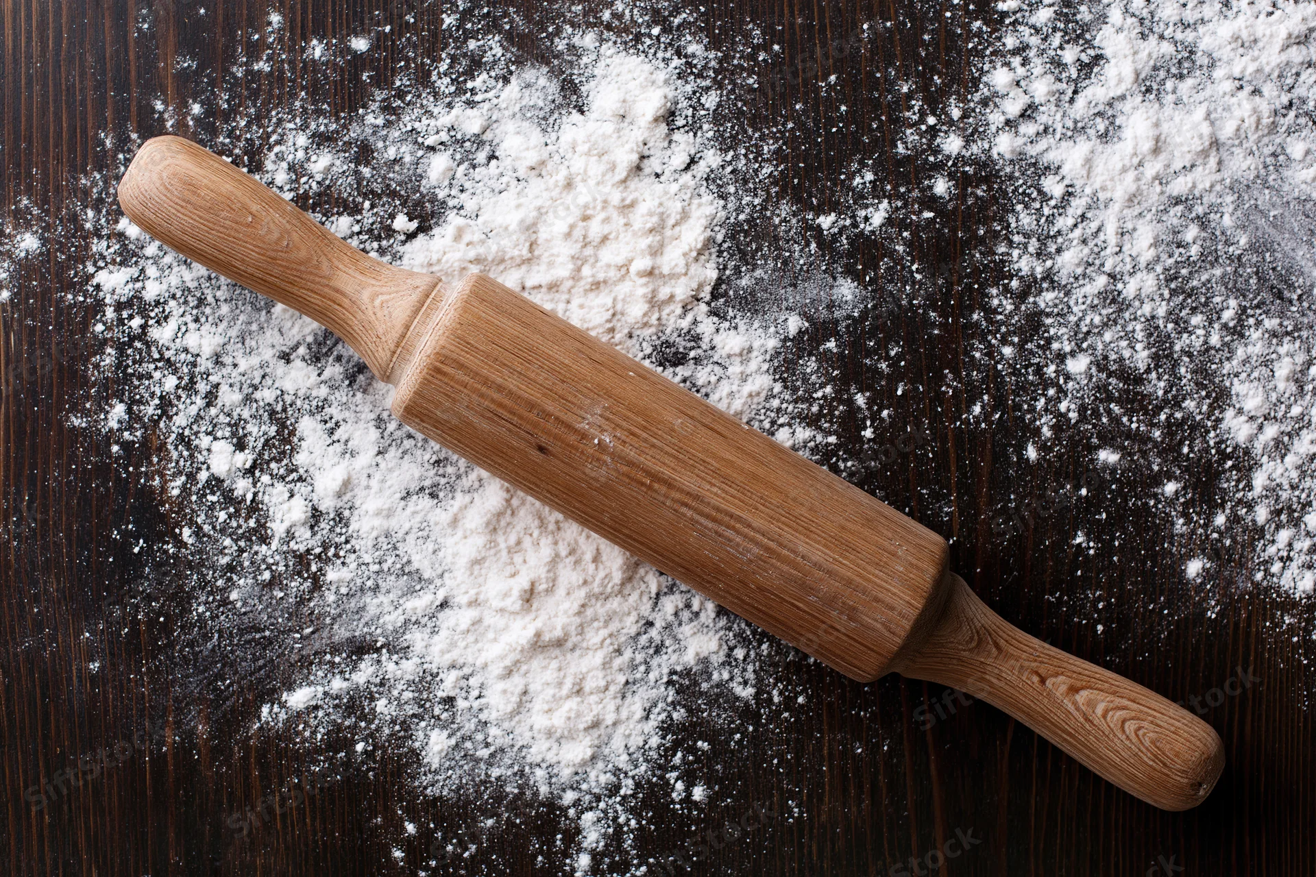 Wooden rolling pin resting on a floured dark wooden surface