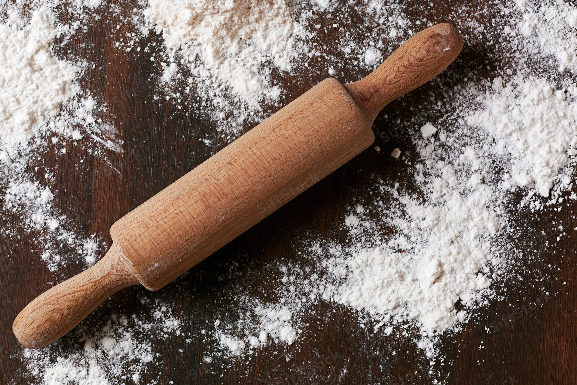 Wooden rolling pin resting on a floured dark wooden surface