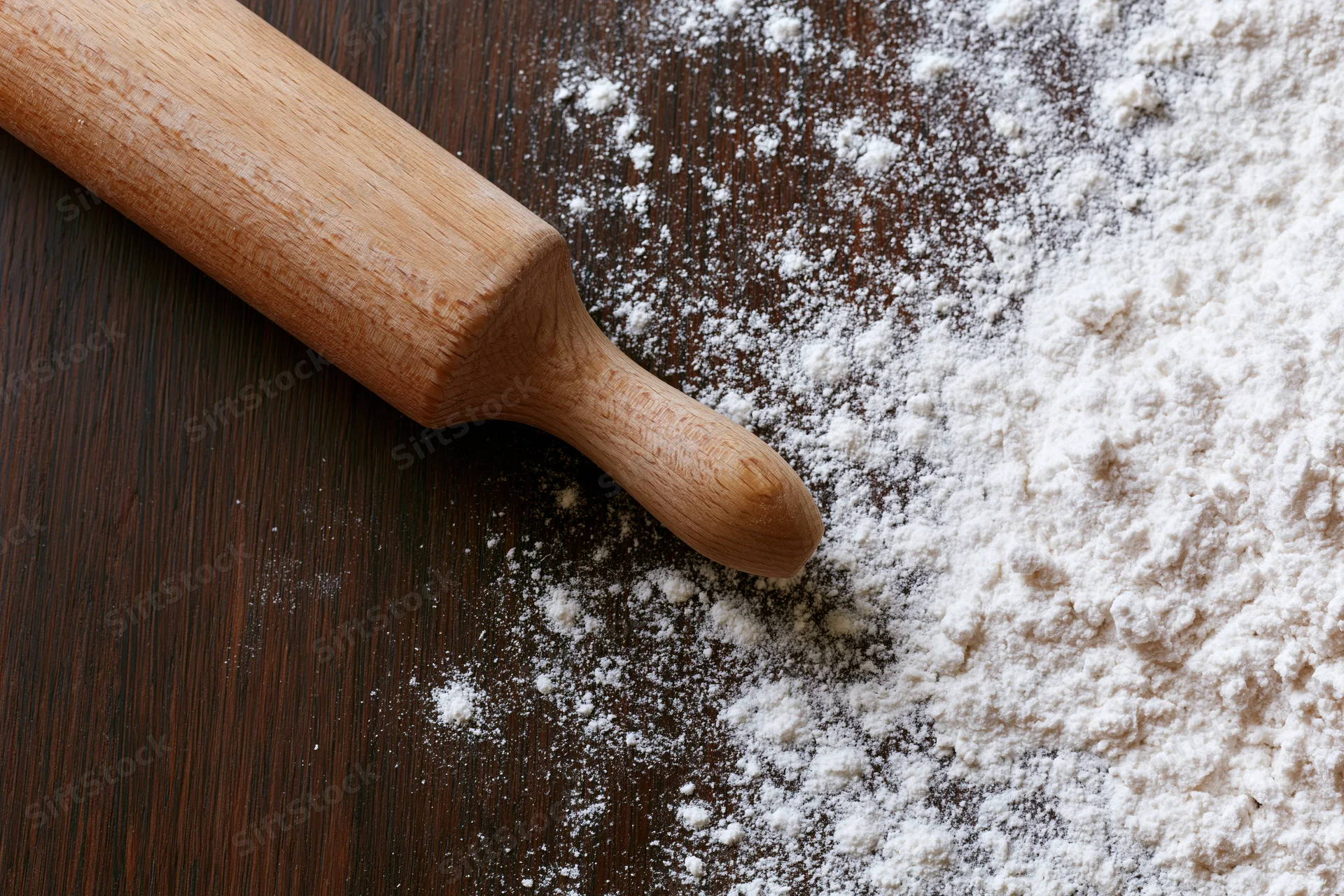 Wooden rolling pin resting on a floured dark wood countertop