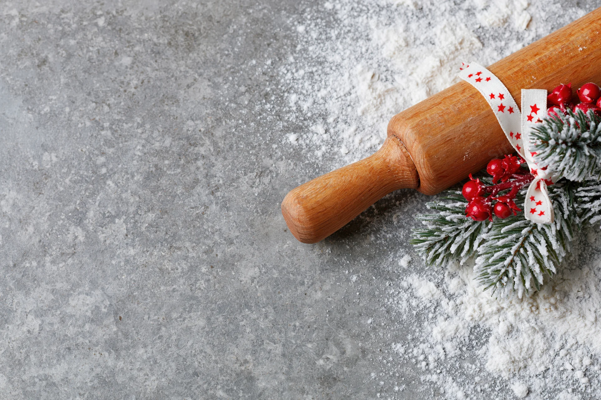 Wooden rolling pin with festive pine and berries on a floured gray countertop