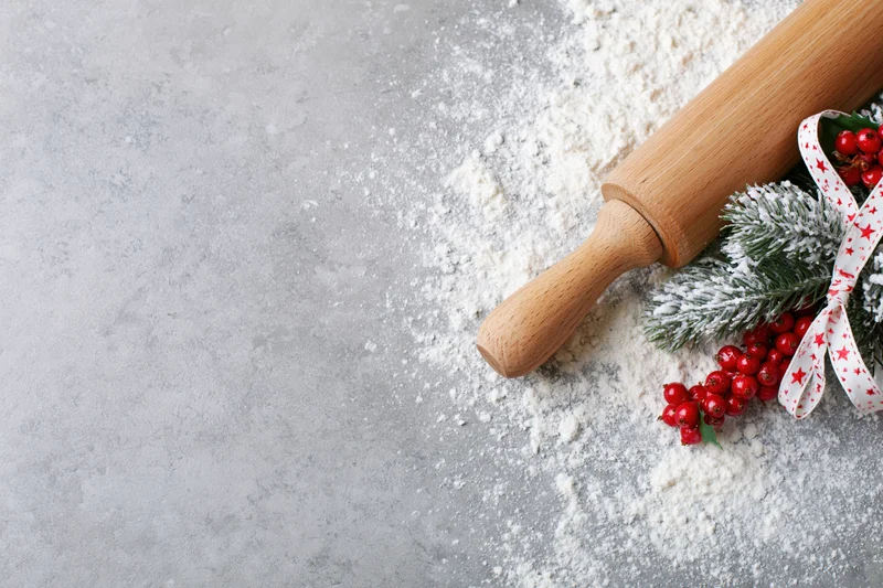 Wooden rolling pin with flour and christmas decorations on gray countertop