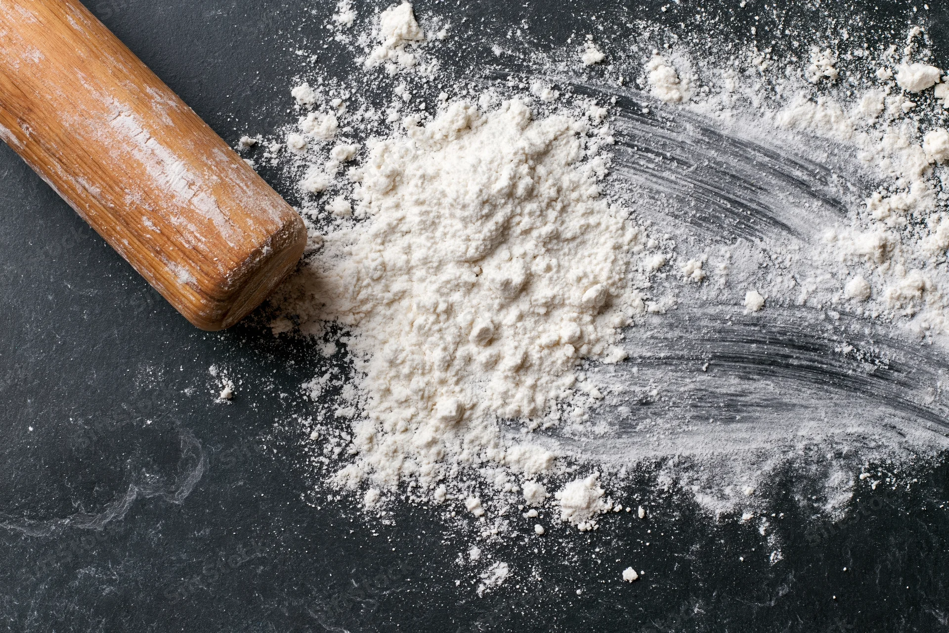 Flour pile with wooden rolling pin on dark countertop