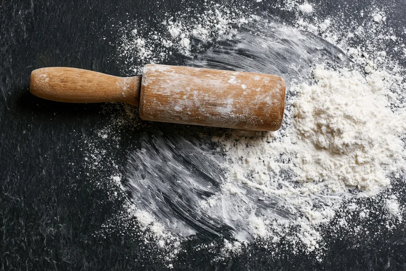 Wooden rolling pin resting on a floured black countertop with scattered flour around it