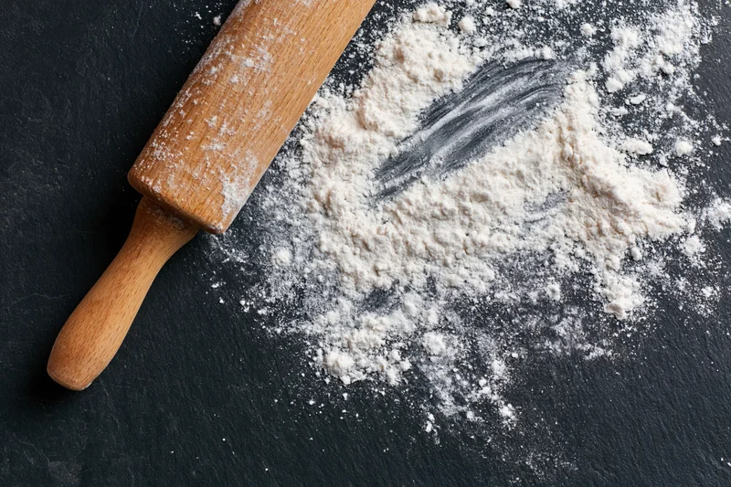 Wooden rolling pin resting on a dark countertop beside a pile of white flour