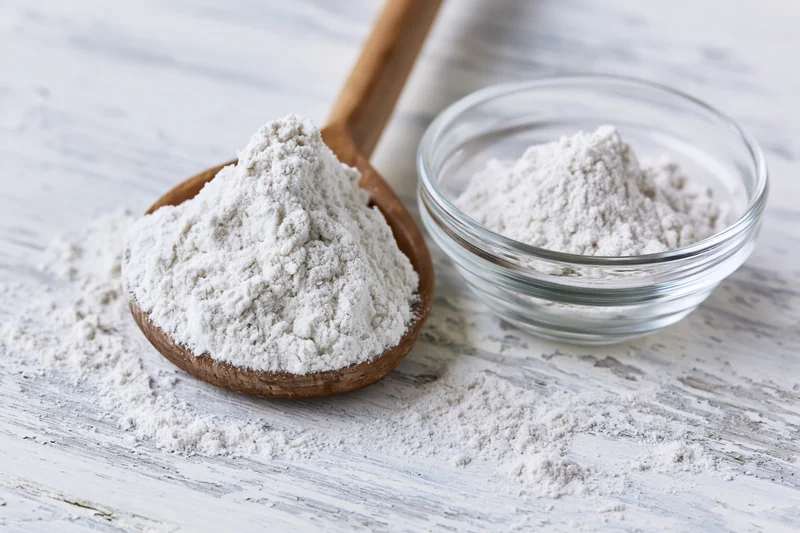 Flour in a wooden spoon and glass bowl on a rustic white table
