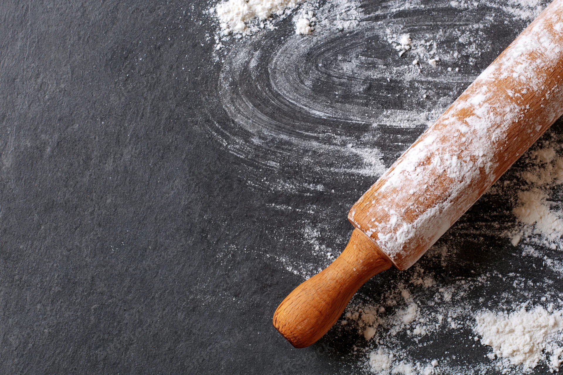 Wooden rolling pin dusted with flour on dark countertop