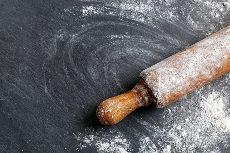 Wooden rolling pin dusted with flour on dark slate surface